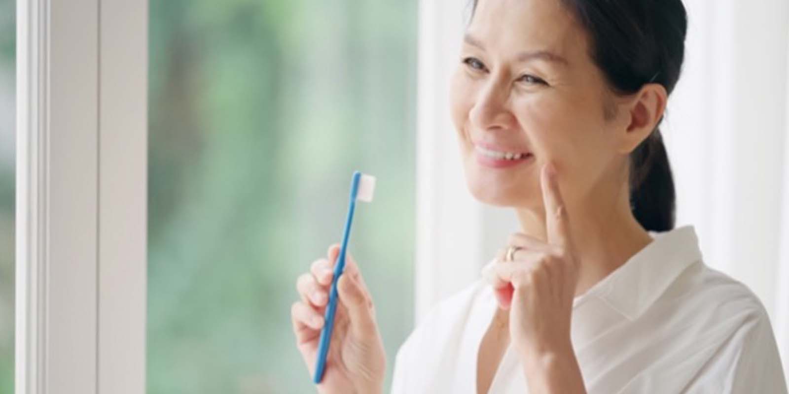 歯ブラシを持ち、もう片方の手の人差し指を口元に当て微笑む女性