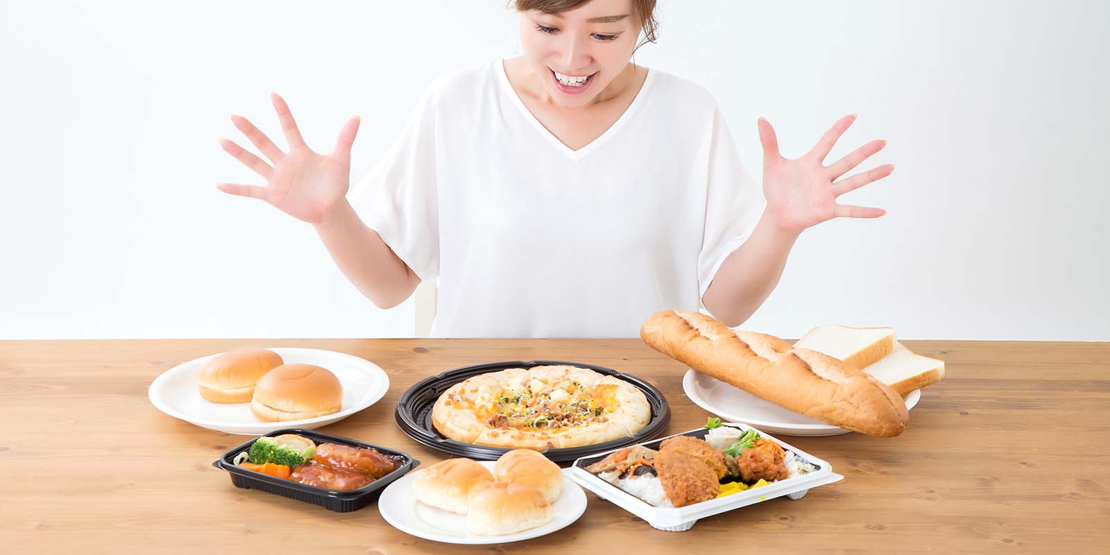 テーブルにパンやピザなどたくさんの炭水化物を並べて喜んでいる女性の写真