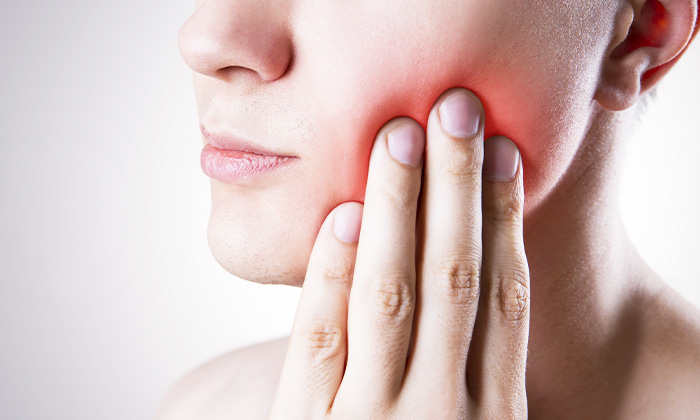 歯が痛み、頬を手でおさえる男性