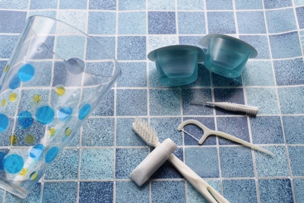 コップと歯ブラシと歯磨き粉、柄付き糸ようじとマウスウォッシュの口腔ケア用品の写真