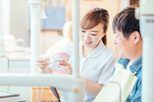 歯科医院で女性スタッフに模型を使って歯磨き指導を受ける男性