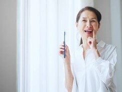 歯ブラシを持ち、もう片方の手の人差し指を口元に当て微笑む女性