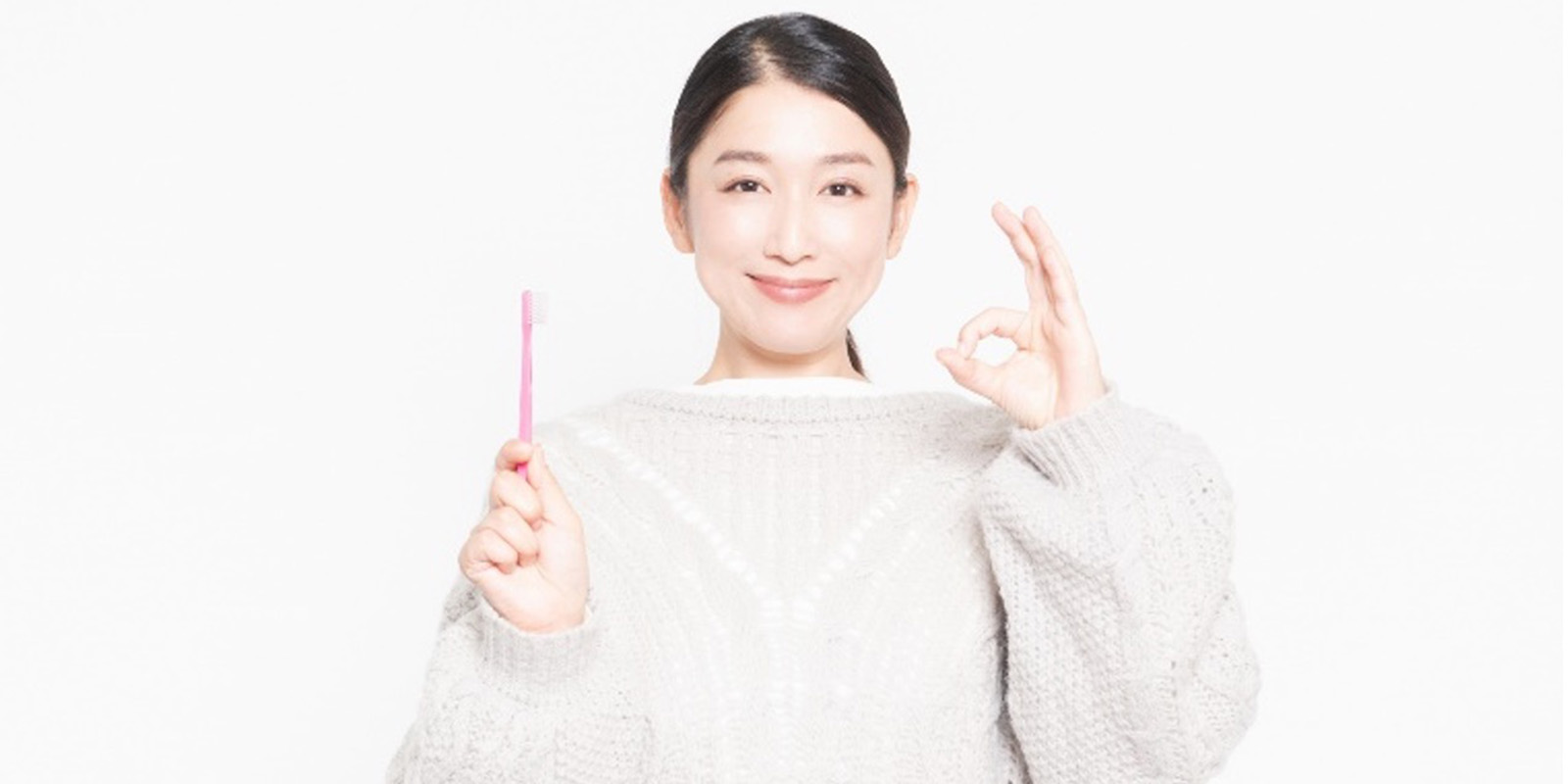 歯ブラシを持ち、OKサインをして微笑む女性