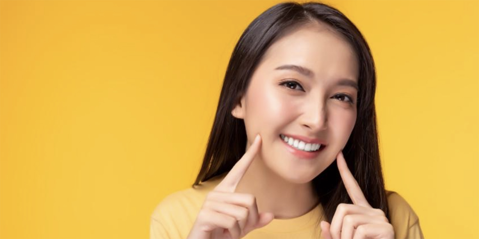 料ての人差し指を頬に当て、白い歯を出し微笑む女性