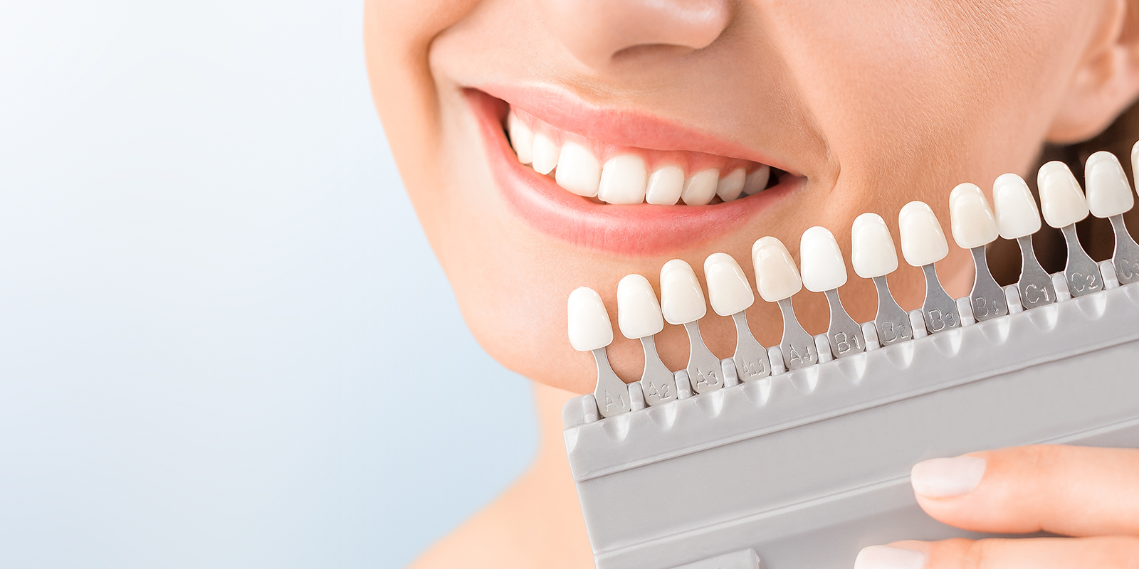 シェードガイドという色を確認するための歯の見本を歯に近づけ、微笑む女性