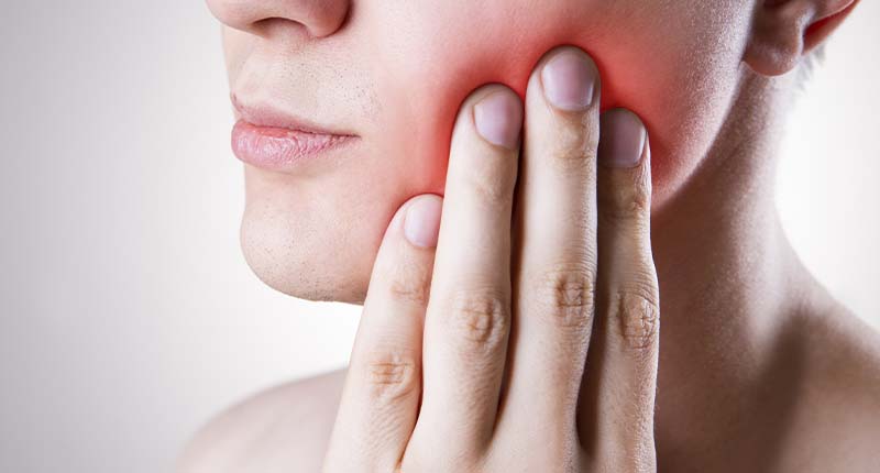 歯が痛み、頬を手でおさえる男性